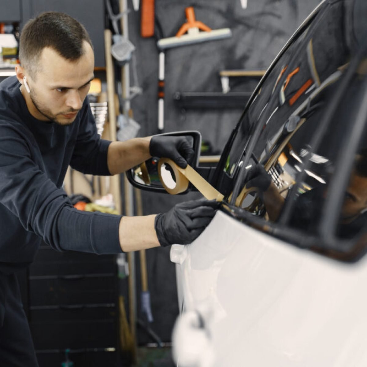 Auto body repair series. Masking car before repaint. Man in a black uniform.
